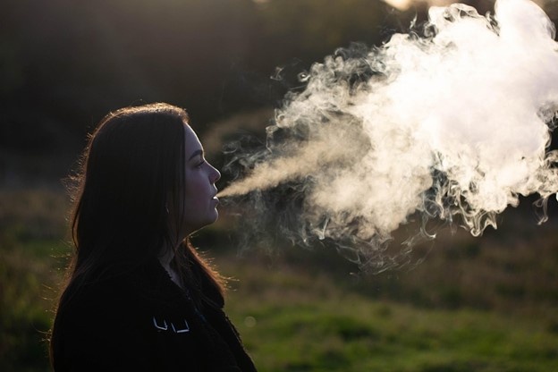 Photo of young adult female blowing vape smoke in nature