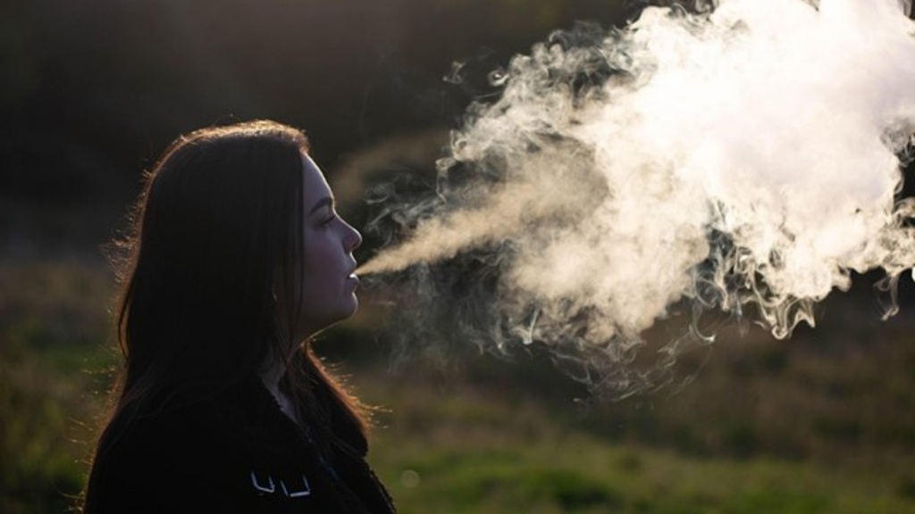 Photo of young adult female blowing vape smoke in nature